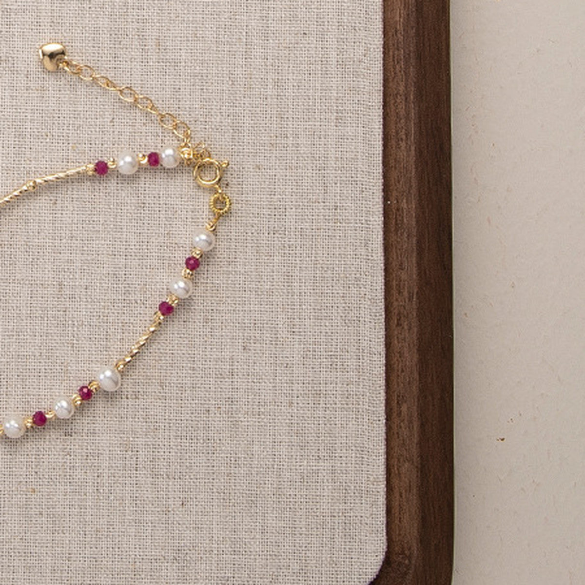 Close detail of the gold heart charm on the pearl and ruby bead bracelet
