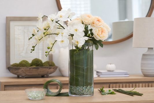Artificial orchids and roses in a clear vase with a leaf wrap and glass beads