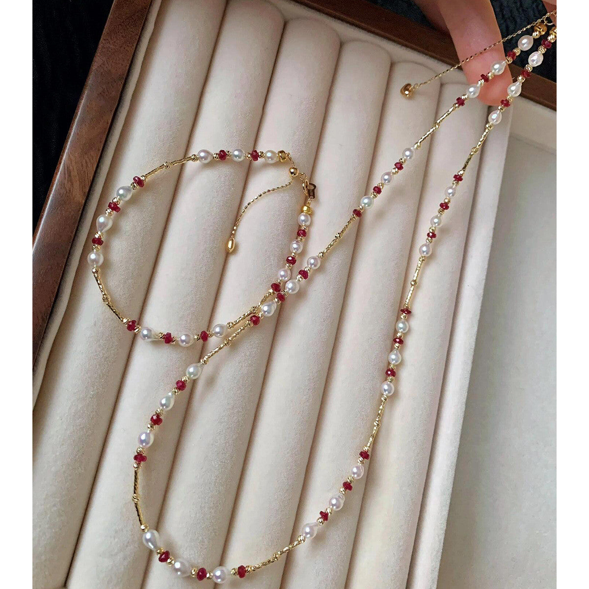 Pearl and ruby-red bead gold-tone necklace on a velvet tray, hand holding the heart-charm extender