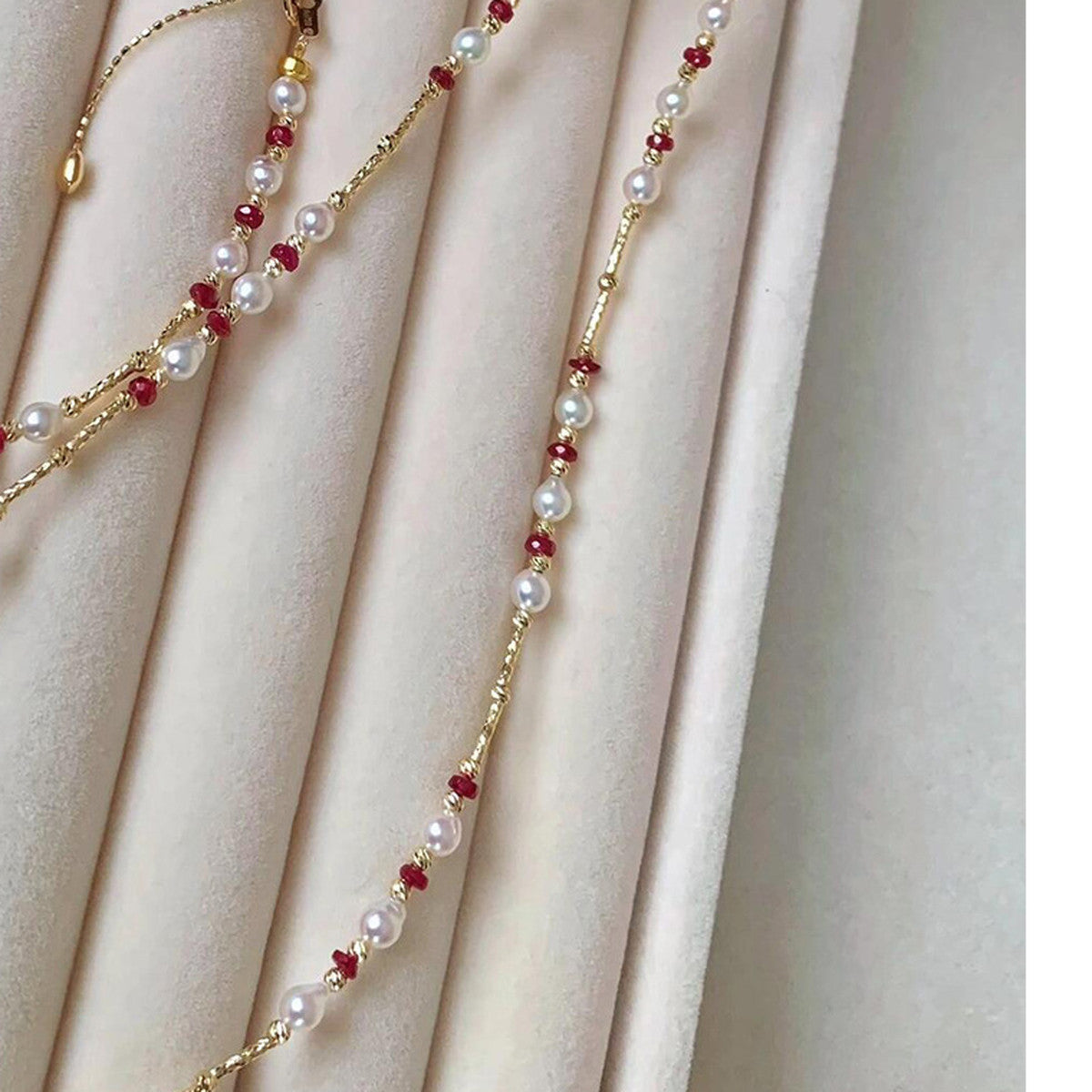 Pearl and ruby bead gold-tone necklace draped on a velvet tray