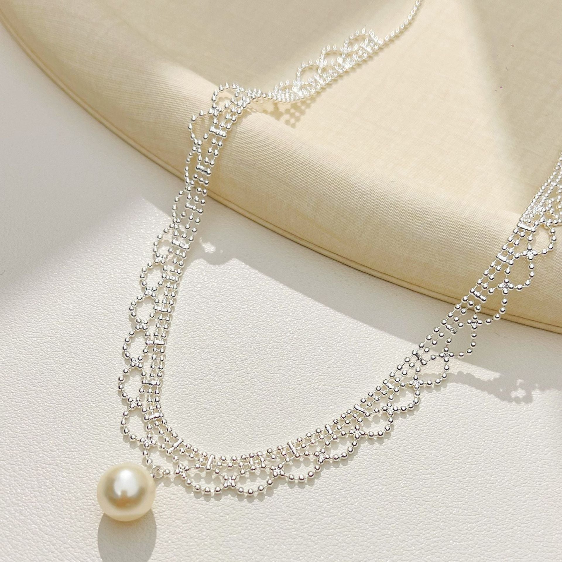 Silver lace pearl drop necklace draped on a tray
